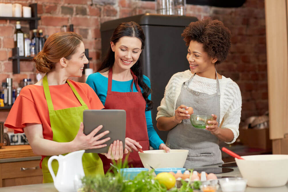A diverse group of women at a cooking class looking at an ipad.