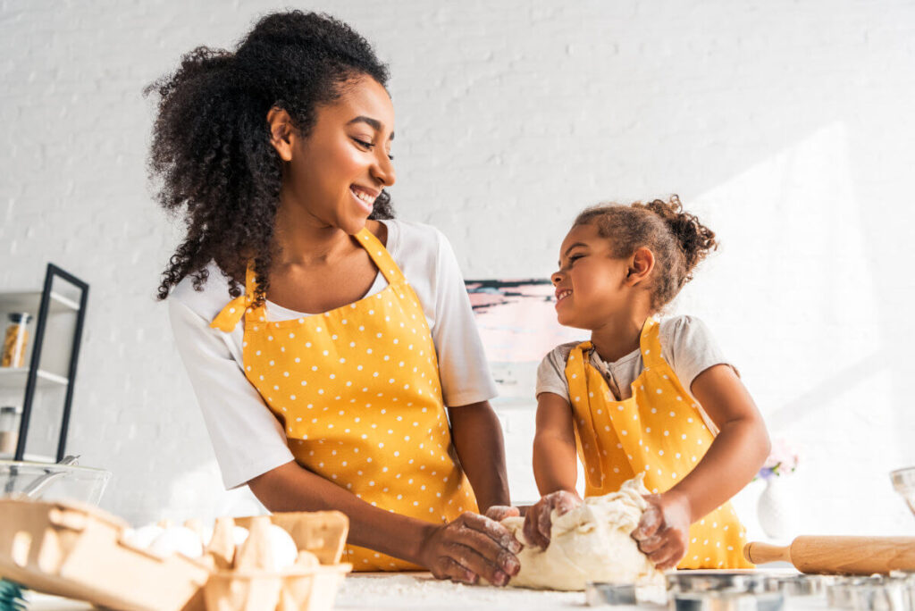 African American mom and daughter smiling and baking bread together.